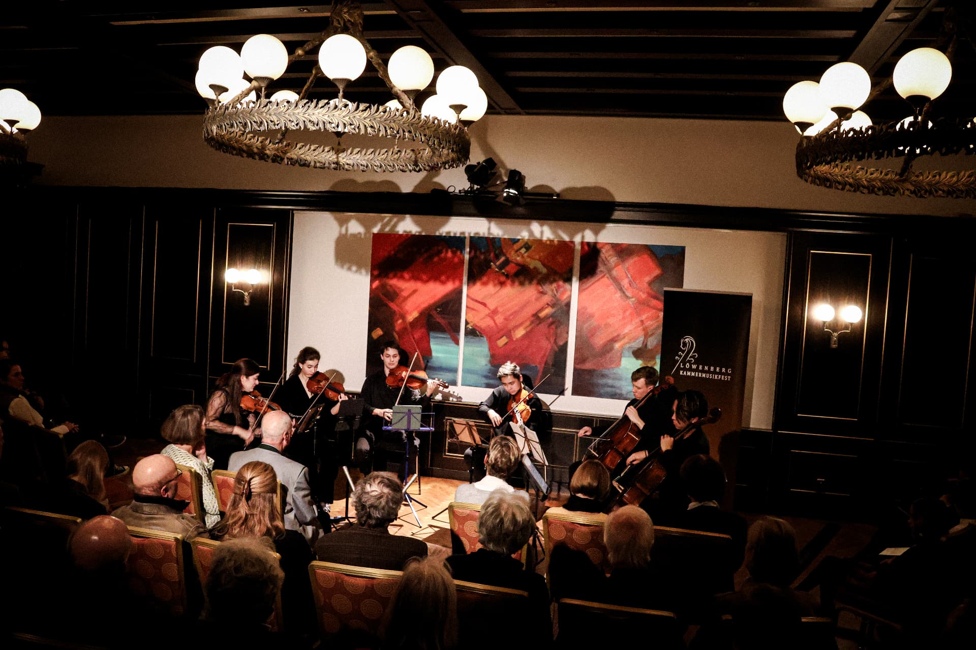 The ensemble performing together in a chandelier-lit hall