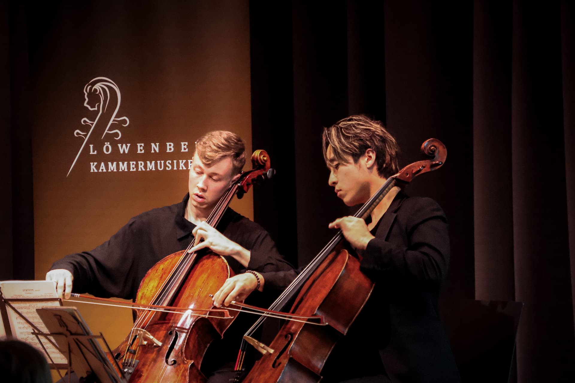 Two cellists performing in front of the festival banner